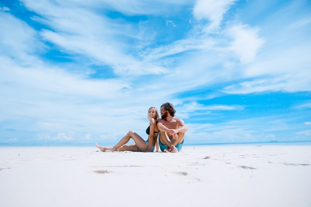 Woman and man sitting on the beach, leaning on each other